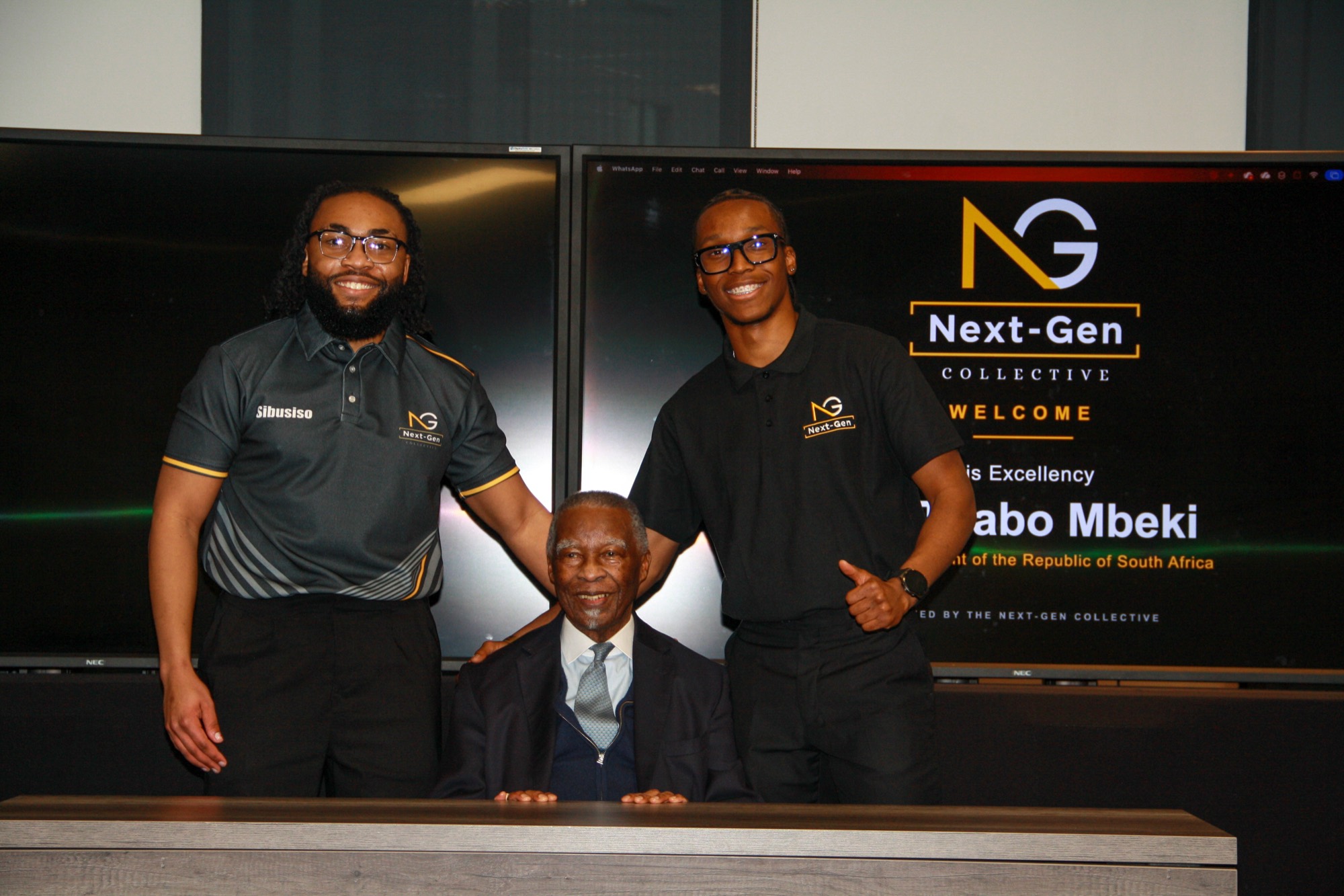 Two founders standing with His Excellency Thabo Mbeki beneath the welcome screen